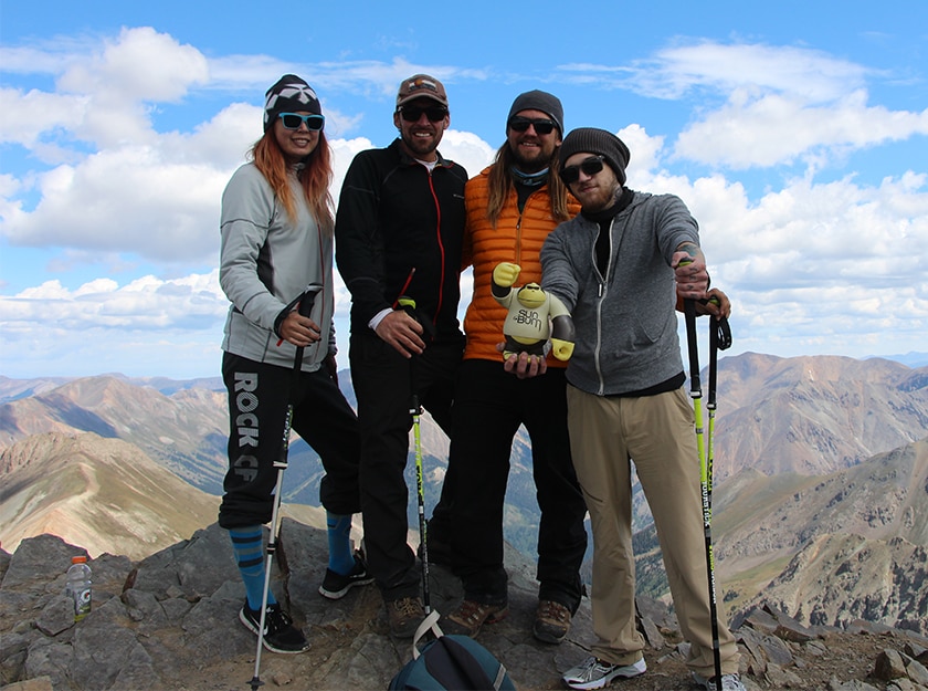 four hikers smiling at top of mountain